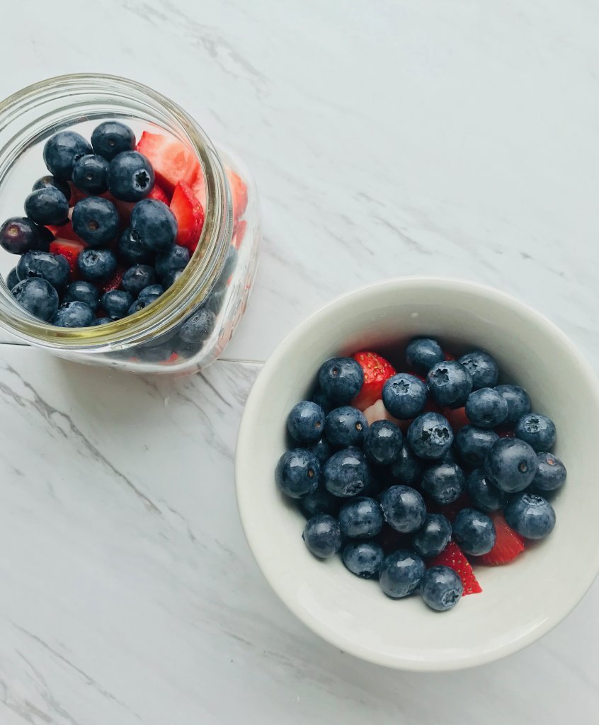 Blueberries on top of strawberries in a glass bowl and white bowl