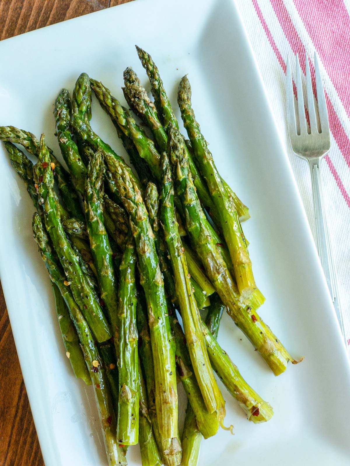 Roasted asparagus on white rectangle dish with a fork next to it