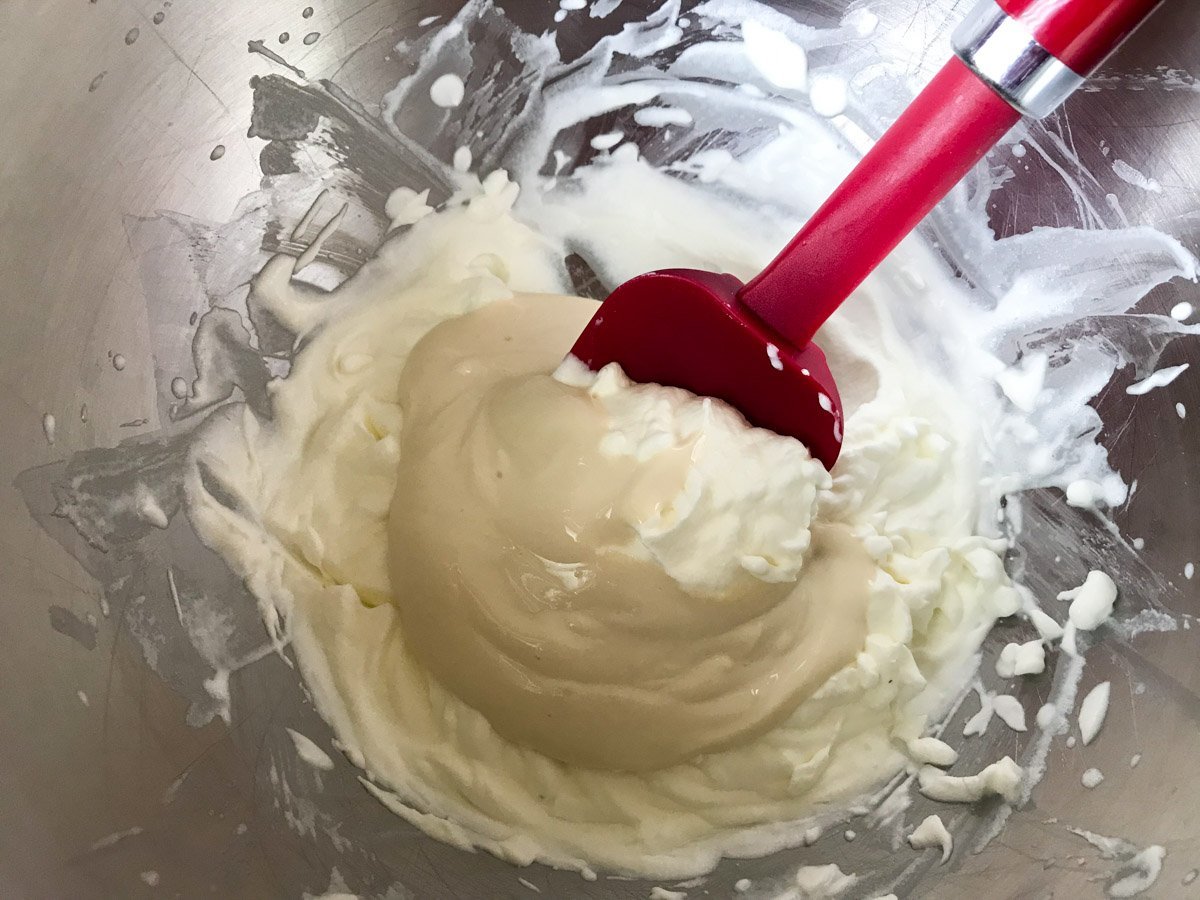 Yogurt and brown sugar mixture on top of whipped cream in a metal bowl with a red spoon
