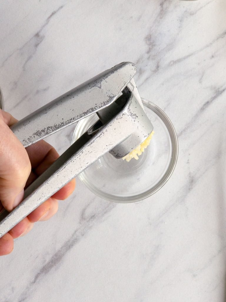 Hand holding garlic press over small glass bowl