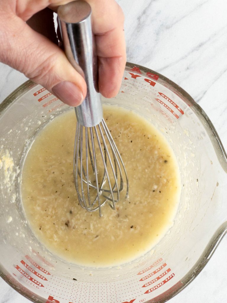 Hand with whisk, Caesar salad dressing in a glass measuring cup