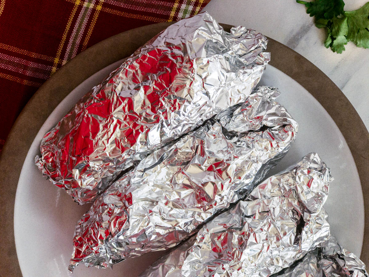 Tacos wrapped in foil on a plate