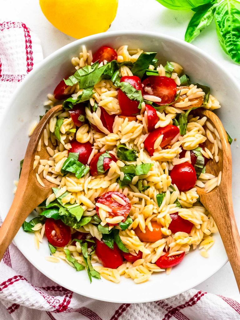 Finished orzo pasta salad with tongs in a bowl