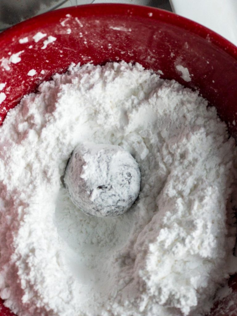 Rolling rum ball in powdered sugar in a red bowl